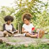 Two kids reading a book while sitting on the ground