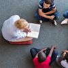 Students sitting on the ground and the teacher is reading